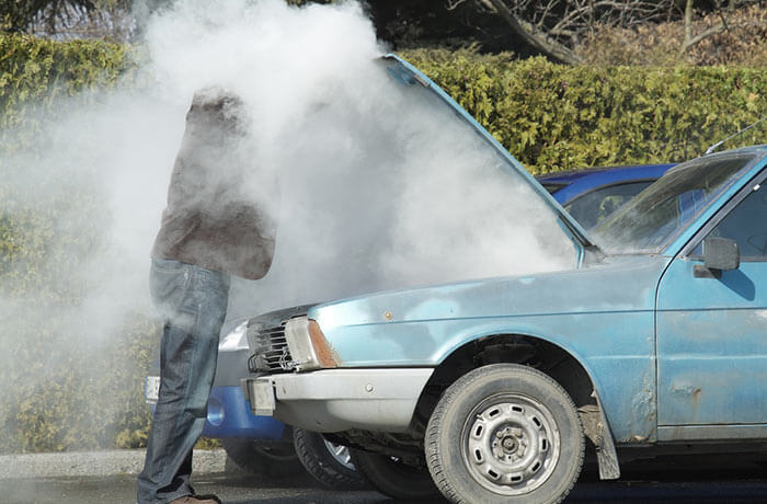An overheated car with smoke pouring out of it